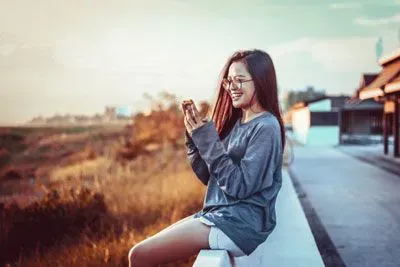 Young woman sitting outside by field scrolling through Tinder on her phone