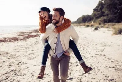Happy couple on a beach walk, man carrying woman piggyback