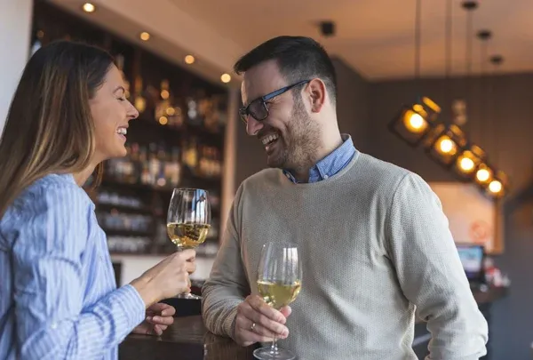 Smiling man and woman holding wine glasses at a wine bar date arranged by a matchmaker.