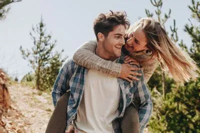 man and woman on a hike; man is giving the woman a piggyback ride