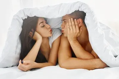 Man and woman under the blanket making kissy faces at each other