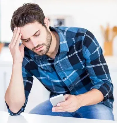 Man with his head in his hand, staring at cell phone and looking frustrated