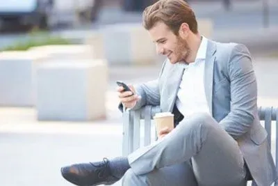 Man sitting on a bench with coffee and his mobile
