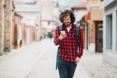 Man walking down street wearing a backpack and smiling at his cell phone