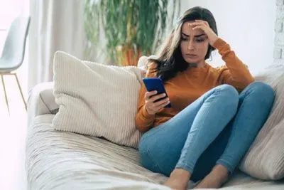 Woman sitting on couch looking skeptical at Tinder on her phone