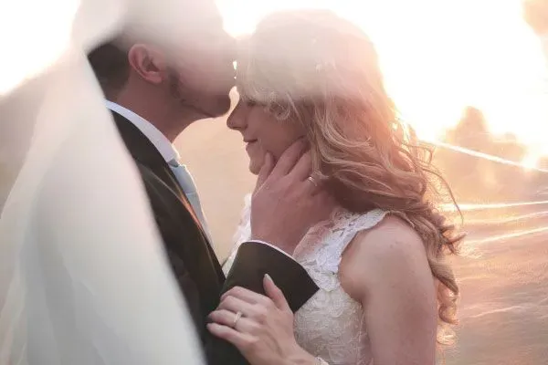 New husband kissing his bride on the forehead with sunshine in the background