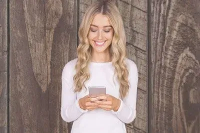 Pretty blonde woman holding her mobile phone in her hands, looking down and smiling