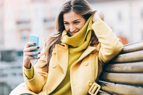 Woman sitting on bench outside and smiling at her smart phone