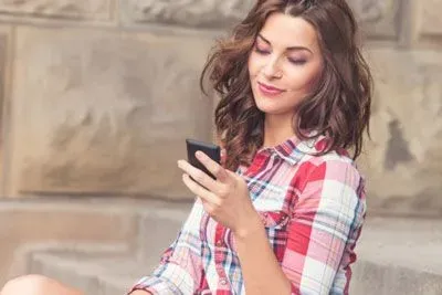 Woman in a plaid shirt checking Hinge on her phone