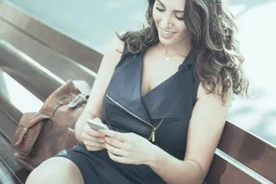 Woman reading Tinder icebreaker on her phone while sitting on a park bench